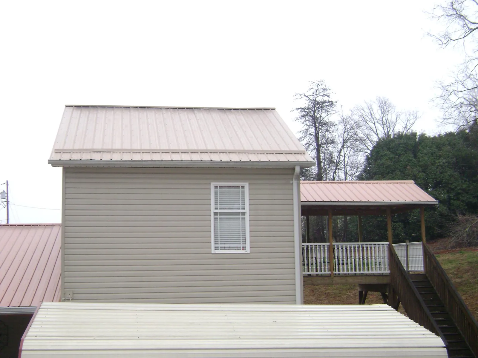 Tan metal roofs on a two story addition and attached porch, from a Roof Replacement job in Bancroft